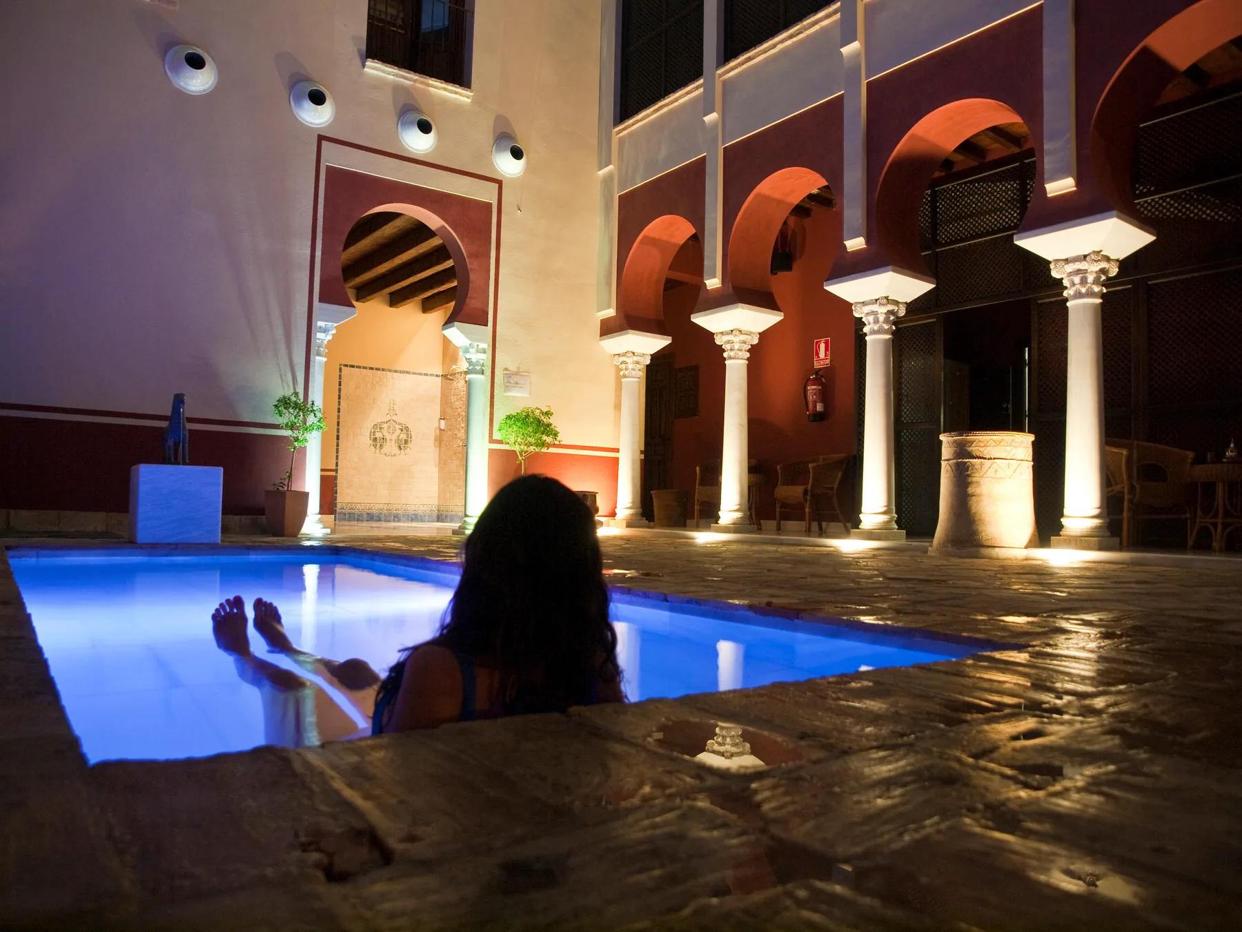 Mujer flotando en piscina nocturna con columnata califal en los Baños Árabes
