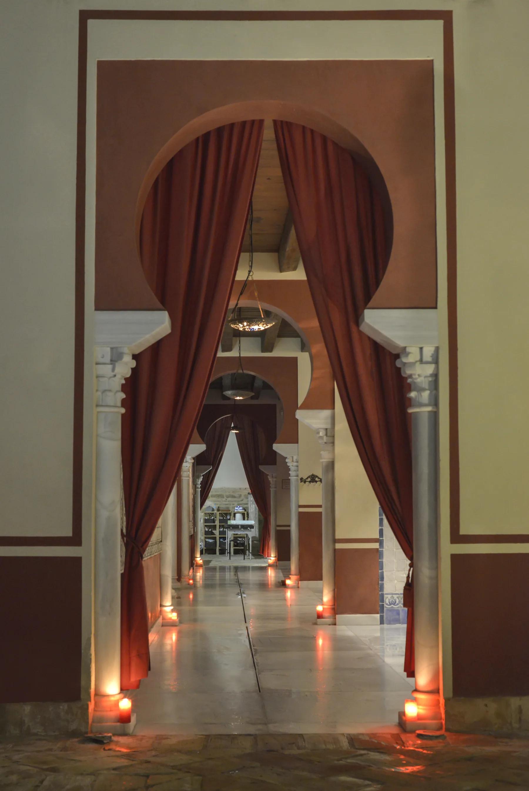 Pasillo con arcos de herradura y cortina granate iluminado por velas