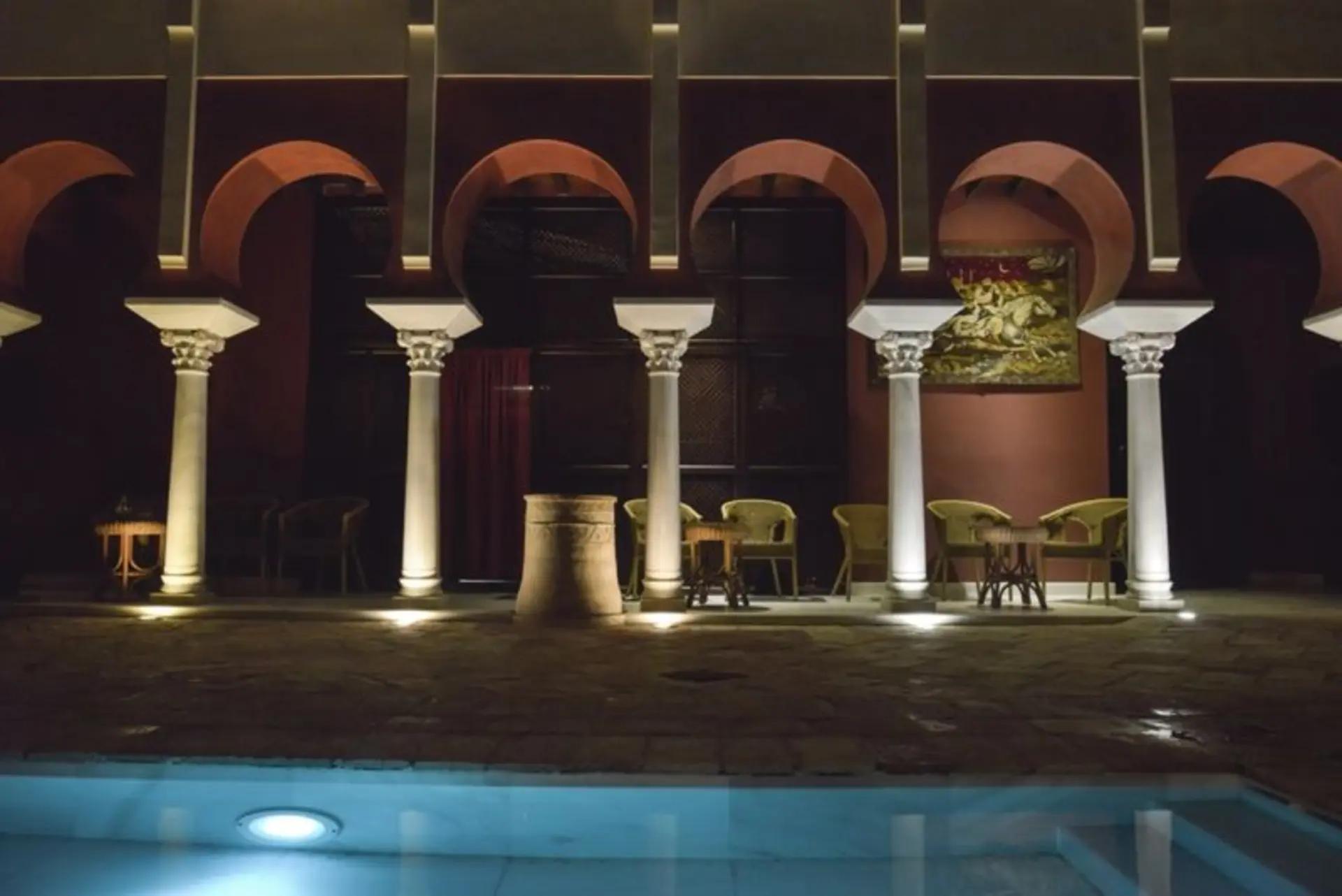 Arcos califales iluminados reflejados en la piscina de noche